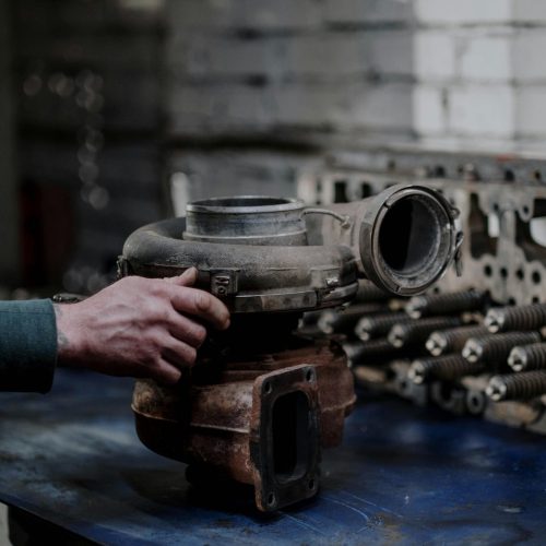 A close-up of a mechanic's hand holding a turbocharger on a workbench in a workshop.